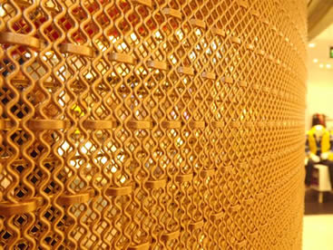 Brass architectural rigid mesh is covering a column.